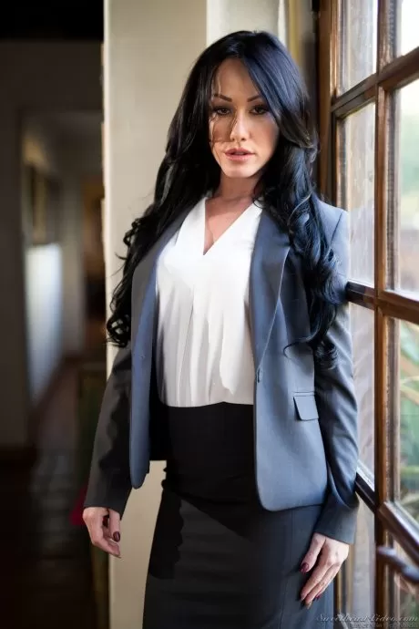 Темноволосая женщина снимает блейзер и юбку, чтобы позировать обнаженной перед окном